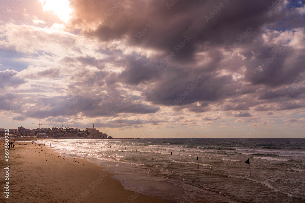 The beautiful sunset on Tel Aviv beach Charles Clore beach with the Mediterranean sea and Jaffa Old City in Israel on a cloudy day.