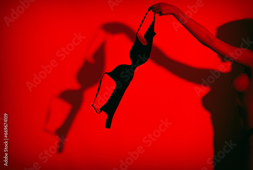 Silhouette of a young sexy girl taking off her bra on a red background.