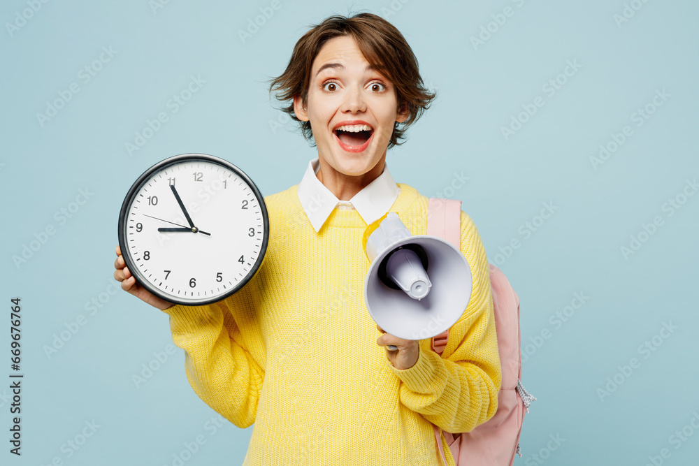 Φωτογραφία Young surprised shocked woman student wear casual clothes yellow sweater backpack bag hold in hand clock scream in megaphone isolated on plain blue background