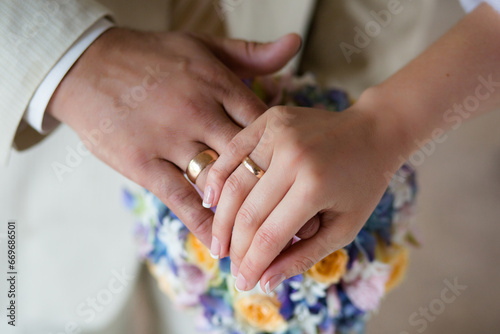 Close-up of newlyweds' hands, with an emphasis on wedding rings, against a background of a flowers.