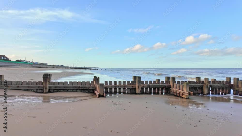 Slow motion panning shot of wooden groynes and sea breakers on the North Norfolk coast. Captured in the seaside village of Ostend on a bright autumn afternoon
