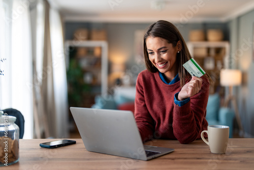 Happy young female entrepreneur using bank card to shop online from home. photo