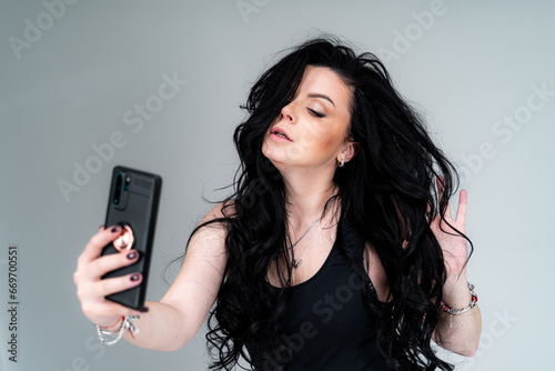 Fashionable Woman With Sleek Hair and Modern Technology in Hand. A woman with long black hair holding a cell phone