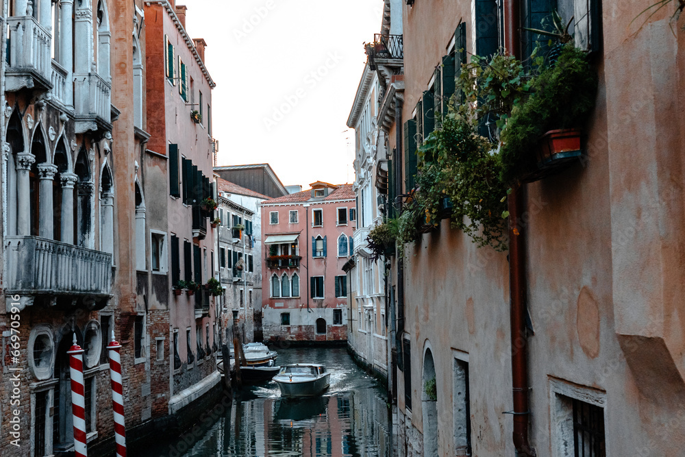Scenic narrow canal with ancient buildings with potted plants in Venice, Italy