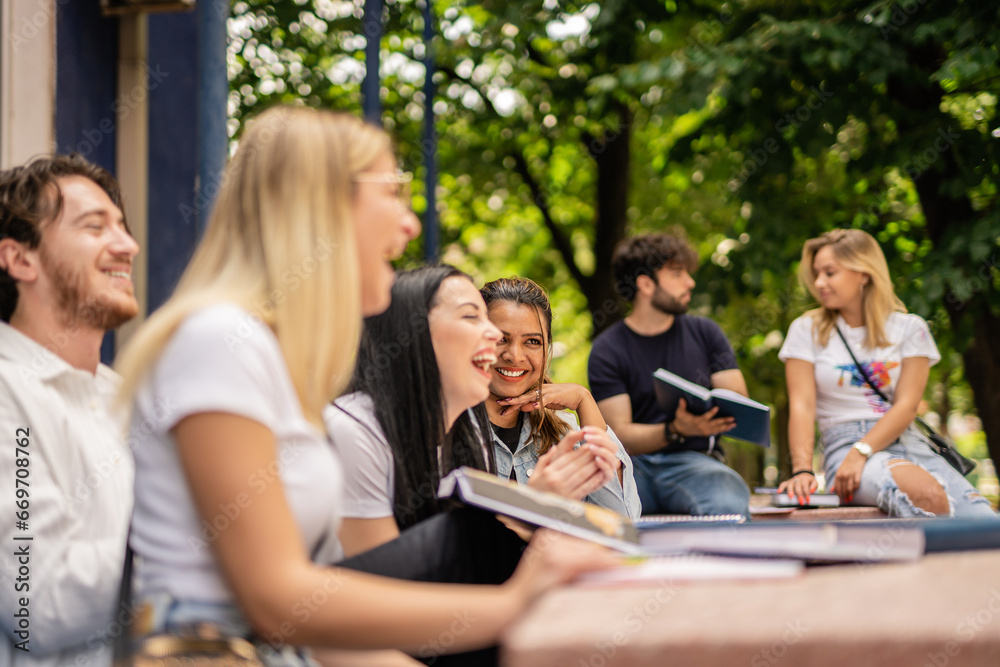 Young, positive, smart students gathered at table in the university yard having fun conversation and laughing Young, positive, smart students gathered at table in the university yard having fun conversation and laughing