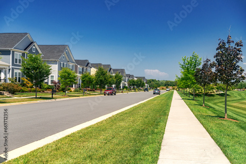 Quiet street in a residential area in the suburbs. Rows of houses along the sidewalk with a green lawn.