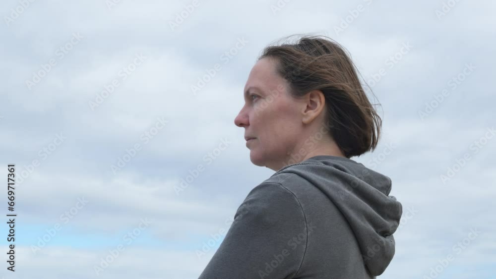 Side view of serious adult female brunette in her 40s standing outdoors and thinking Side view of serious adult female brunette in her 40s standing outdoors and thinking
