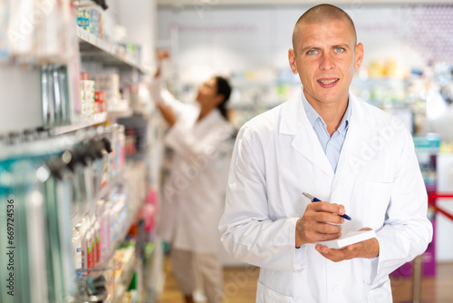 Positive pharmacist makes notes on a notebook in the sales area of a pharmacy