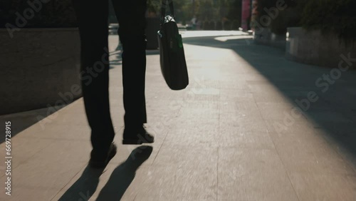 In this dynamic video, a tracking shot provides a close-up of a young man's legs, walking with style in the city's business district. With a wallet in hand, photo