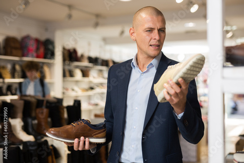 Interested male shopper choosing comfortable casual shoes, comparing two moccasins models in store photo