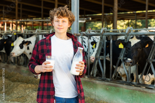 Young man is standing with glass of milk and bottle mailk at the cow farm photo