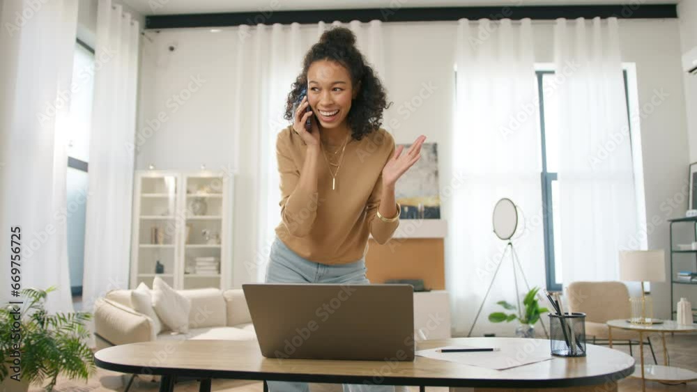 Young adult Afro American female entrepreneur working on laptop and speaking with client or partner on smartphone in home office. Positive small business owner managing project and multi tasking 4K Young adult Afro American female entrepreneur working on laptop and speaking with client or partner on smartphone in home office. Positive small business owner managing project and multi tasking 4K