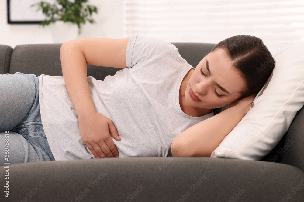 Woman suffering from abdominal pain while lying on sofa at home. Unhealthy stomach Woman suffering from abdominal pain while lying on sofa at home. Unhealthy stomach