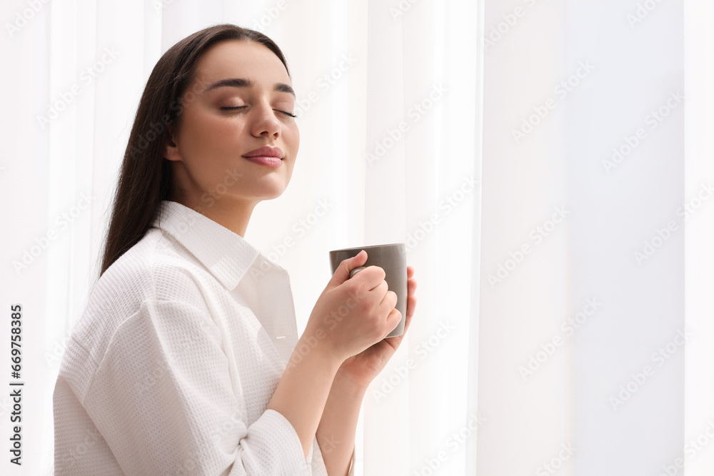 Beautiful woman with cup of drink near window at home, space for text. Lazy morning Beautiful woman with cup of drink near window at home, space for text. Lazy morning
