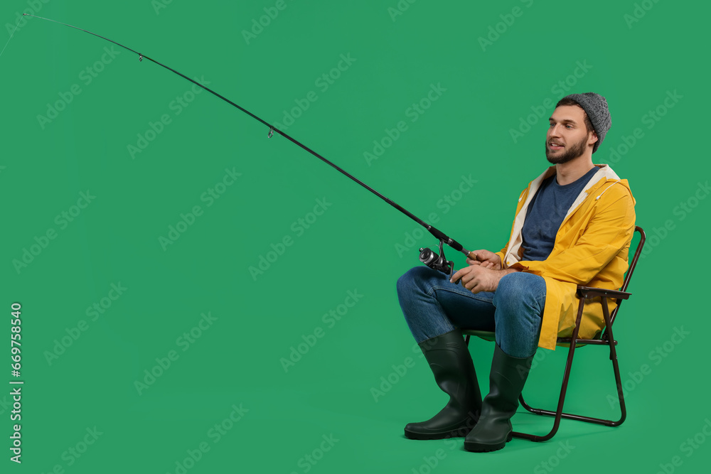 Fisherman with fishing rod on chair against green background, space for text Fisherman with fishing rod on chair against green background, space for text