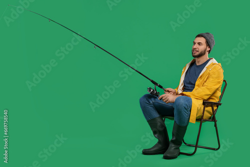Fisherman with fishing rod on chair against green background, space for text