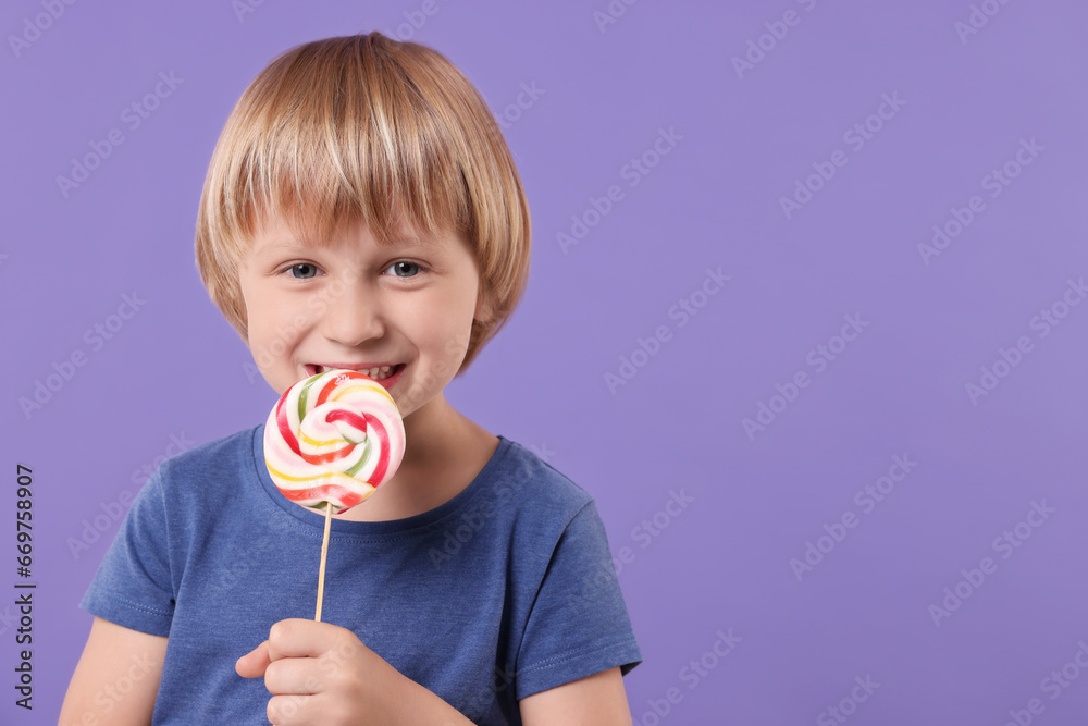Happy little boy licking colorful lollipop swirl on violet background, space for text Happy little boy licking colorful lollipop swirl on violet background, space for text