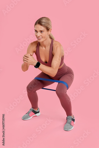 Woman exercising with elastic resistance band on pink background