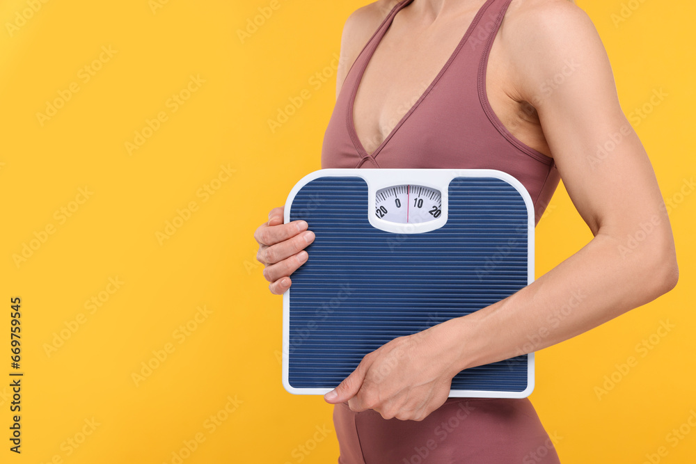 Slim woman holding scales on yellow background, closeup and space for text. Weight loss - obrazy, fototapety, plakaty 