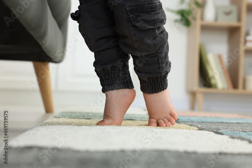 Baby standing on soft carpet near sofa, closeup