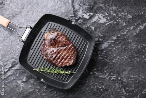 Grill pan with delicious fried beef meat and rosemary on grey textured table, top view. Space for text