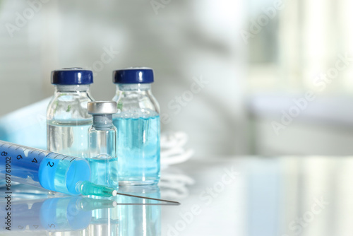 Glass vials, syringe and medical masks on white table, closeup. Space for text