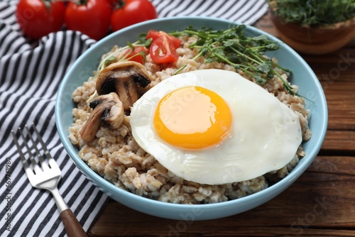 Tasty boiled oatmeal with fried egg, mushrooms and tomatoes served on wooden table, closeup