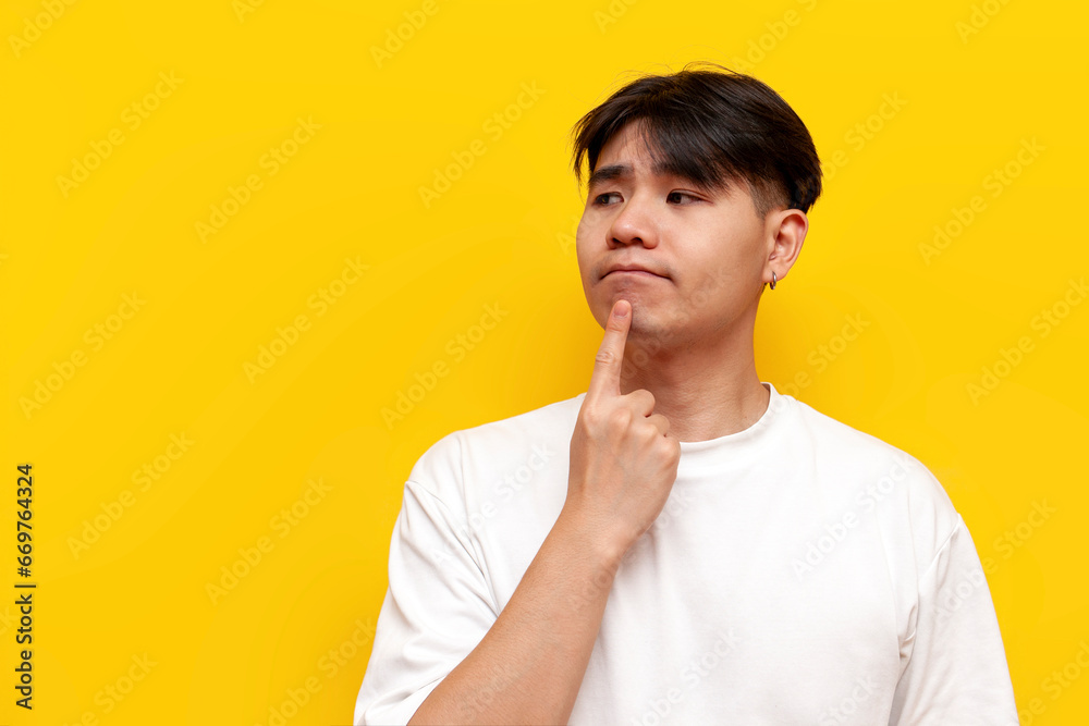 pensive asian guy in white t-shirt thinking and planning over yellow isolated background, puzzled korean man daydreaming pensive asian guy in white t-shirt thinking and planning over yellow isolated background, puzzled korean man daydreaming