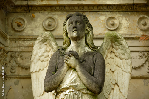 winged angel with folded hands on a historical tomb looks up to heaven expectantly