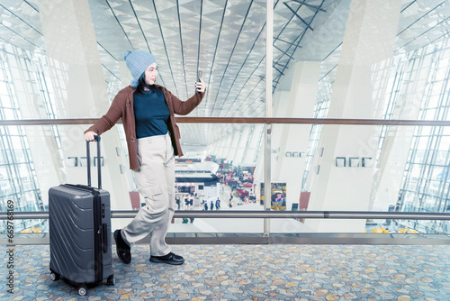 Full length photo of Asian woman taking a self portrait with a suitcase at the airport