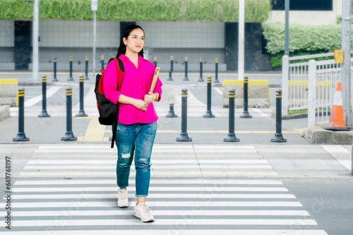 Full length front shot of an Asian female student in jeans with a backpack crossing the road