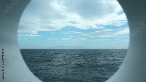 View from round deck window to sea. Clip. Beautiful seascape with mountain coast on horizon from round window. Sea voyage and view from round window