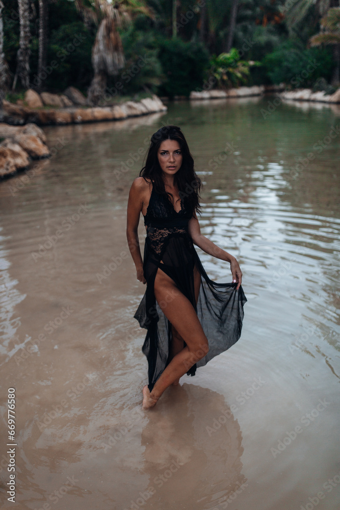 Fototapeta premium Beautiful woman at the lake between palms at the evening