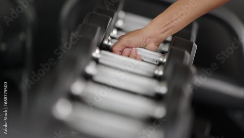 Slow motion close up of woman picking up free weight from dumbbell rack at fitness center