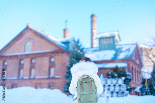 Woman tourist Visiting in Sapporo, Traveler in Sweater looking Sapporo Beer Museum with Snow in winter season. landmark and popular for attractions in Hokkaido, Japan. Travel and Vacation concept photo