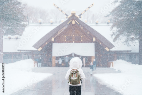 Woman tourist Visiting in Sapporo, Traveler in Sweater looking Hokkaido Shrine with Snow in winter season. landmark and popular for attractions in Hokkaido, Japan. Travel and Vacation concept