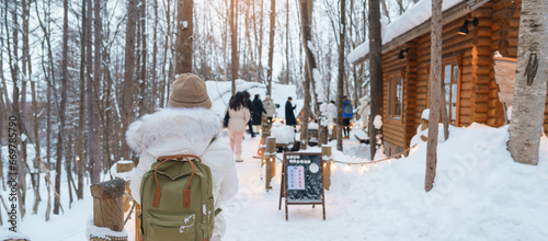 Woman tourist Visiting in Furano, Traveler in Sweater sightseeing Ningle Terrace Cottages with Snow in winter. landmark and popular for attractions in Hokkaido, Japan. Travel and Vacation concept photo