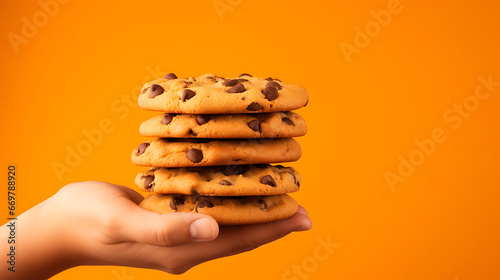 a hand holding chocolate chip cookies on an orange background with textspace