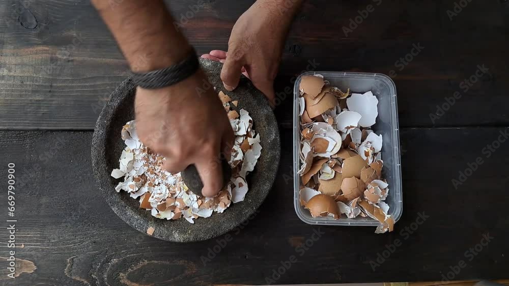 A man's hand is crushing an egg shell using a mortar. Pounded eggshells can be used as fertilizer.	