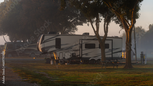 Rv motorhome parked at campsite early morning with sunlight shineing on vehicle 