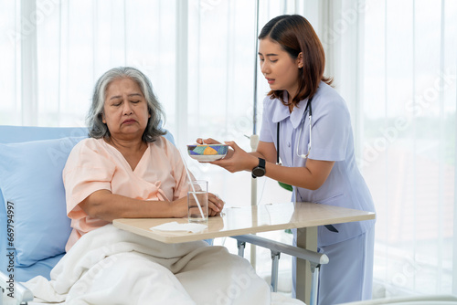 A nurse cares for and feeds an elderly Asian patient but she has anorexia.