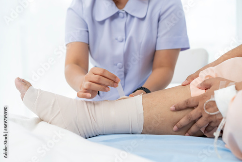 Close-up photo of an Elderly Asian patient admitted to hospital A nurse cares for a patient's injured leg bandage.