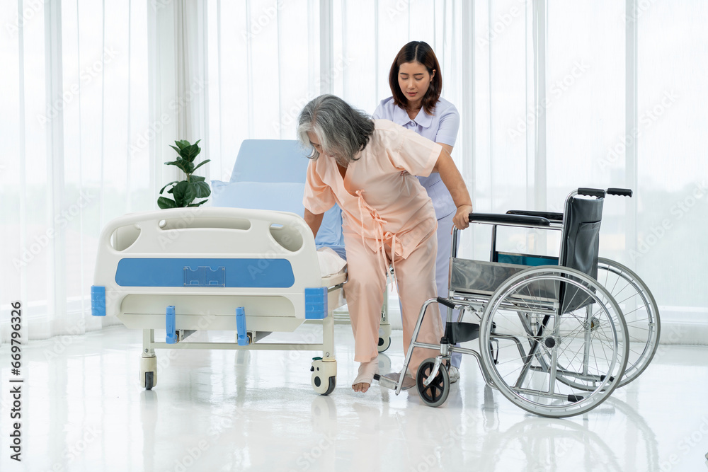 A nurse carries an elderly Asian patient from a wheelchair onto a bed after taking him for an x-ray of his leg injured in an accident.