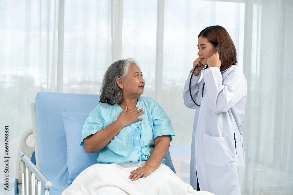 Fototapeta premium Female doctor uses stethoscope to check lung breathing for elderly Asian female patient.