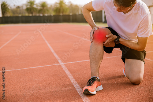 Fit man runner has twisted ankle injury while practice marathon run at the racetrack.