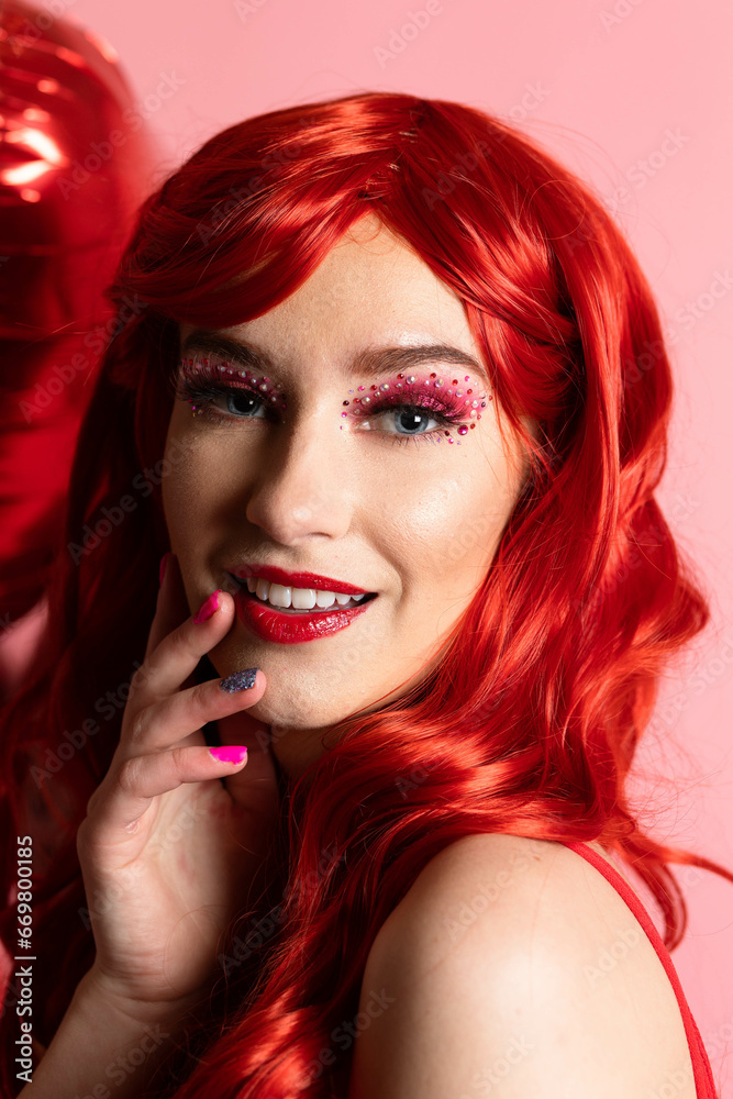 Fototapeta premium Beautiful Young Women with Scarlet Red Hair Posing with Valentine's Decor in a Hot Red Jumper