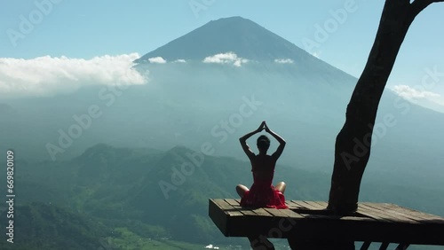 Aerial 4K Drone Footage: Serene Yoga at Lahangan Sweet, East Bali; Girl in Anjali Mudra Pose on Tree Platform, Gazing at Agung Volcano; Ideal for Wellness Blogs, Meditation, and Travel Videos photo