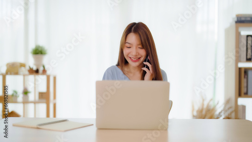 Young asian woman happy working on computer laptop and hand typing chat message on mobile smartphone at home. Video call, Online meeting © Monster Ztudio