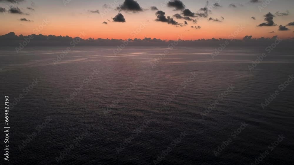 Drone flying backwards during beautiful orange sunrise over calm sea Drone flying backwards during beautiful orange sunrise over calm sea