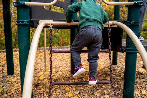 Toddler Boy Climbing on Chain Ladder on Playground in Fall